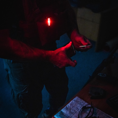 Red tactical LED light in use during night operations, illuminating essential tools for law enforcement. Ideal for map reading and preserving night vision. Military-grade safety beacon used by police and emergency responders. Rechargeable, waterproof design compatible with NVG systems. Perfect replacement for chemlights and traditional flashlights in tactical scenarios, enhancing low-light visibility while maintaining stealth.